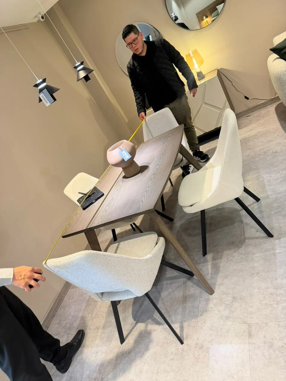 Comedor en madera oscura con sillas blancas en un showroom, tomando medidas
